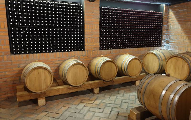 Slika buradi u kojima se čuva vino sa policama na kojima se nalaze vinske flaše