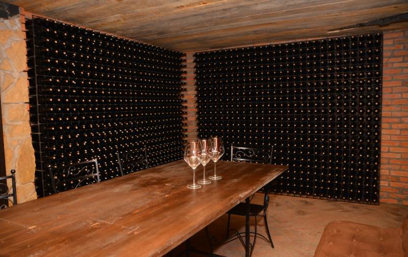 Slika stola na kome su tri vinske čaše sa belim vinom i u pozadini su police sa vinskim flašama